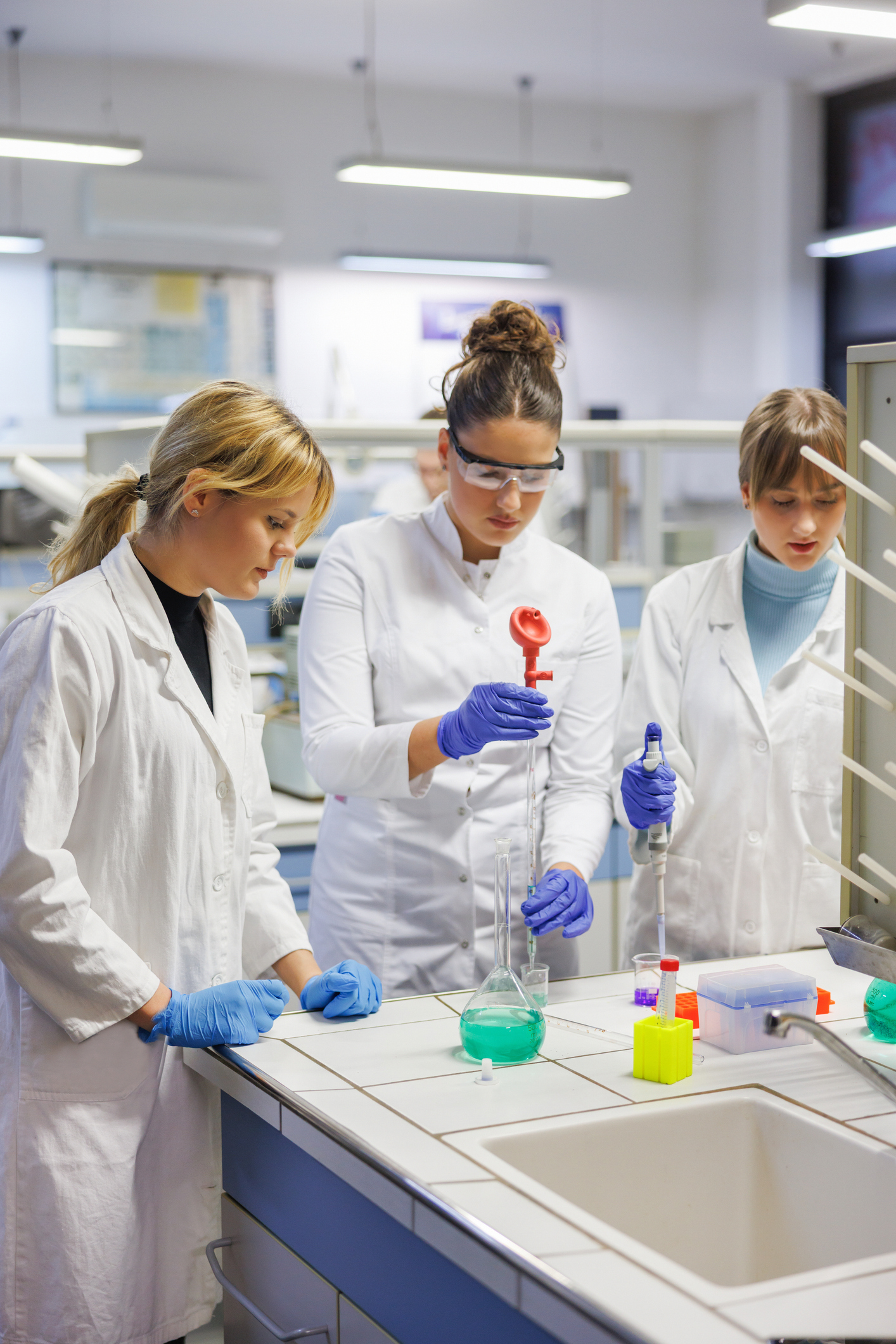 Female students in lab coats, protective eyewear and gloves gloves practicing in lab with chemicals