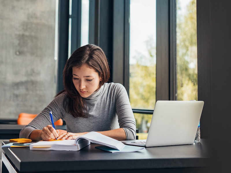 Student taking notes from books at library