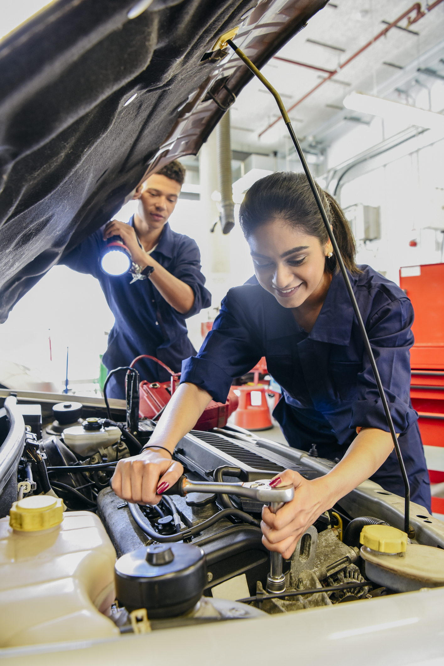 Young female mechanic repairing car, man holding torch
