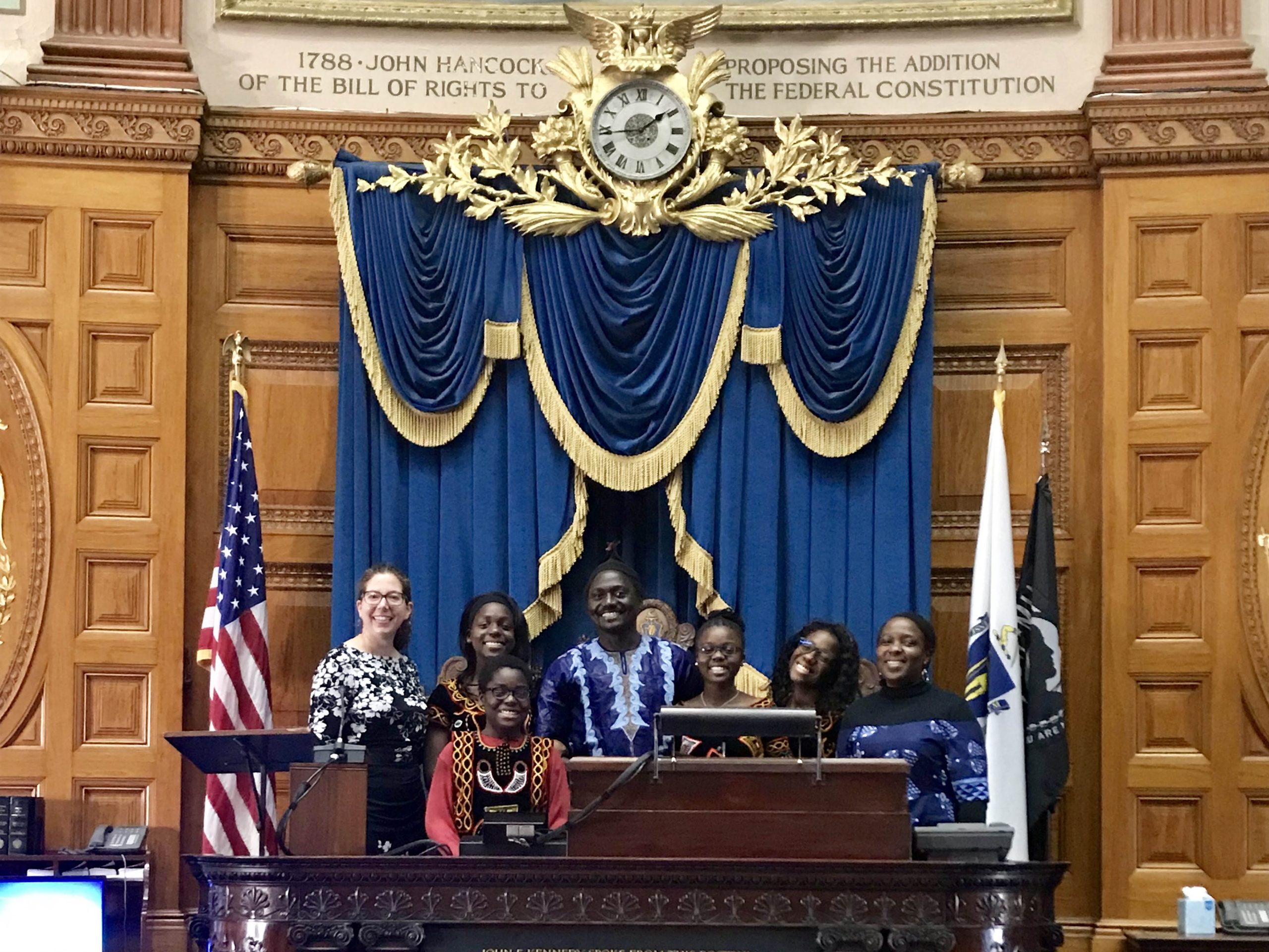 Seven people stand at an official looking podium.