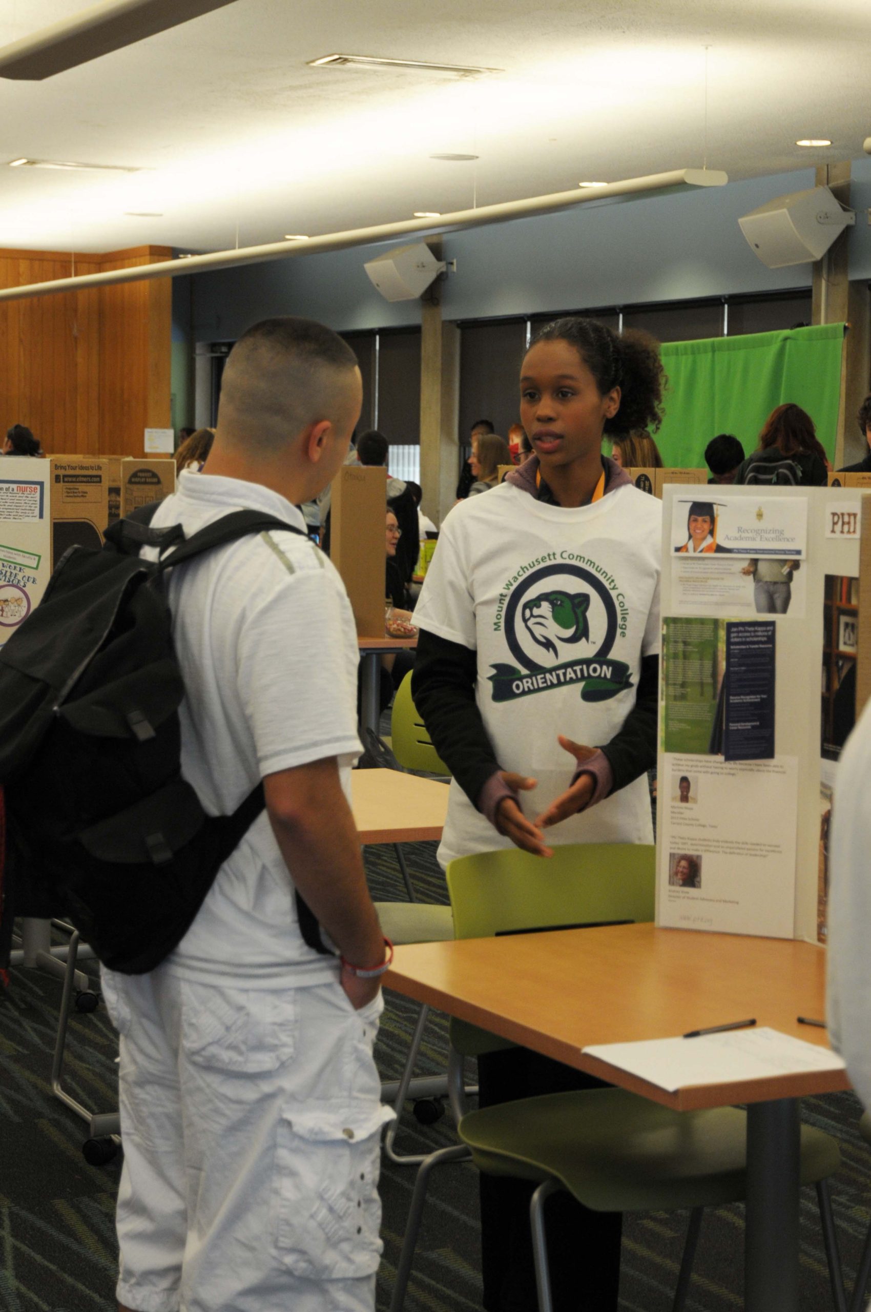 Two students talking together in front of a club presentation board