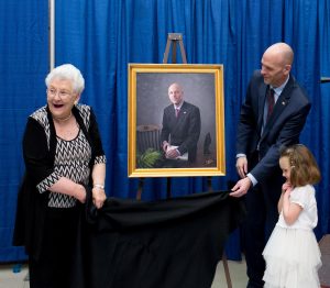 The president, his mother and daughter stand in front of a painting of the president.