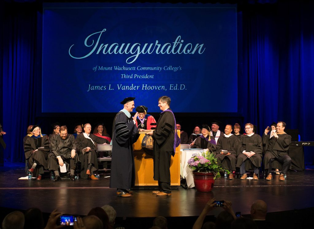 A group of people stand on a stage as President Vander Hooven holds his hand to a copy of the constitution and is sworn in 