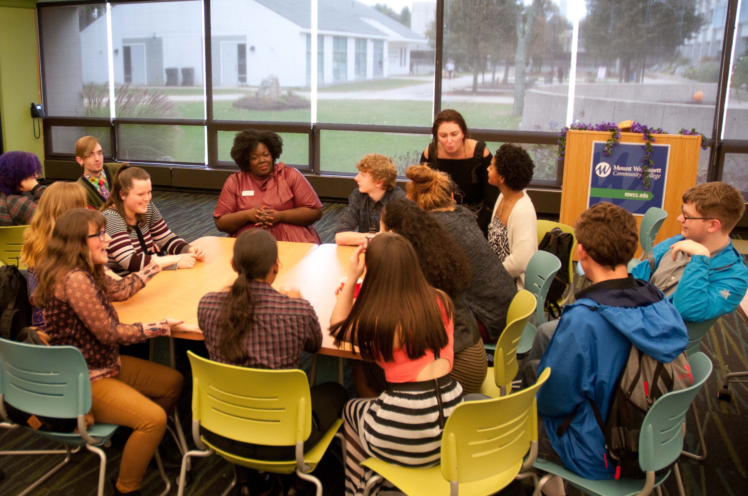 A group of students sits around a teacher as they have a discussion.