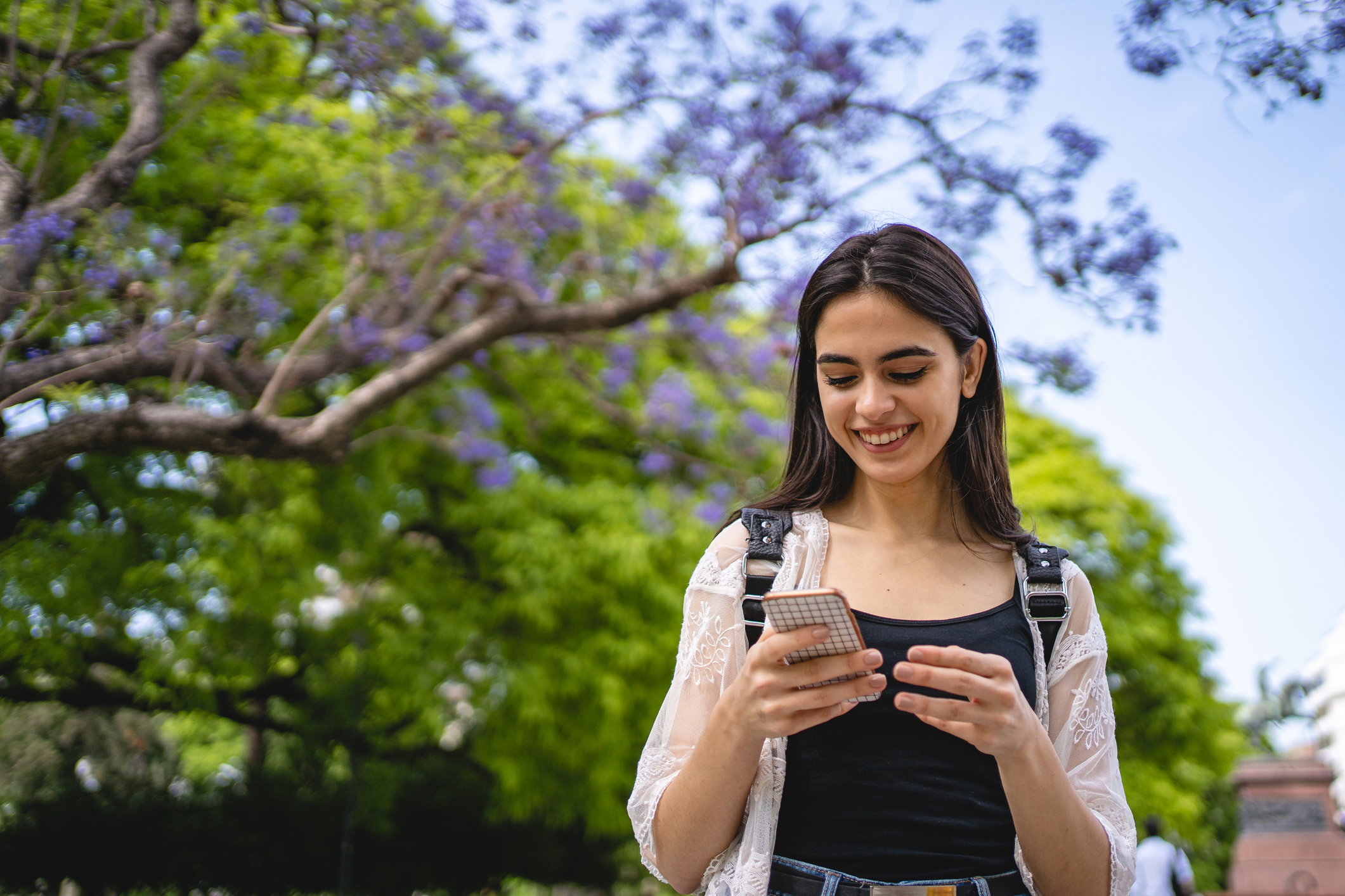 Joyful girl standing in a park while texting