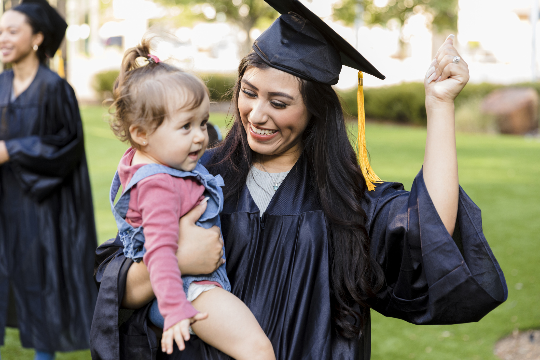 Young adult mom in cap and gown smiles at daughter