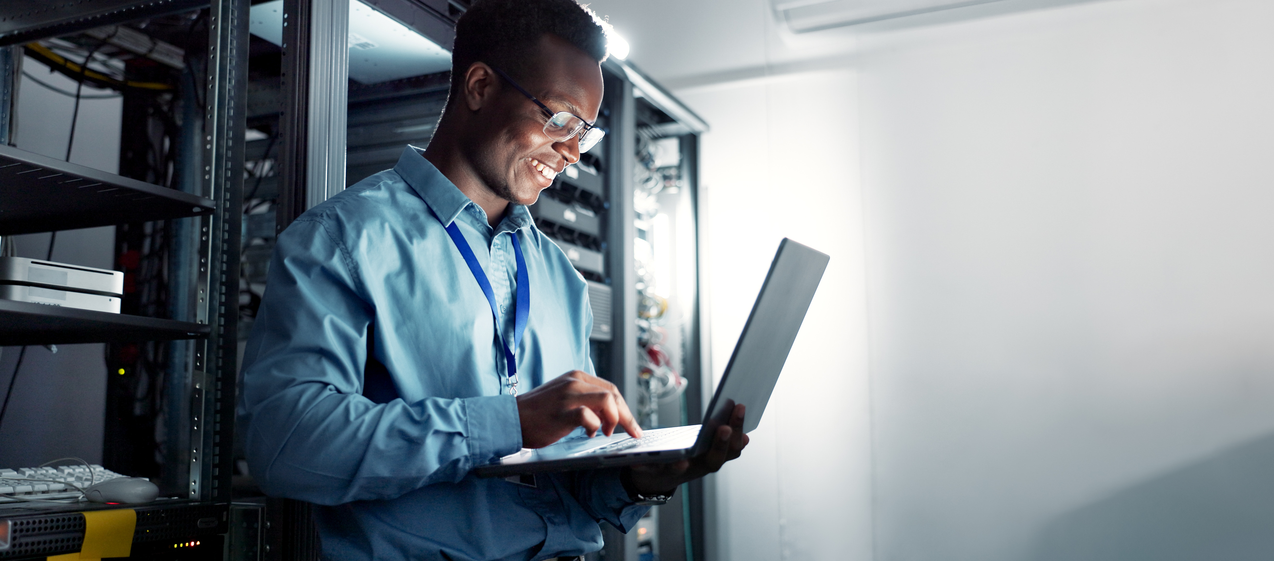 Laptop, server room and black man on network for maintenance, programming software or typing. Tech, data center and happy engineer on system database for information, cybersecurity or cloud computing