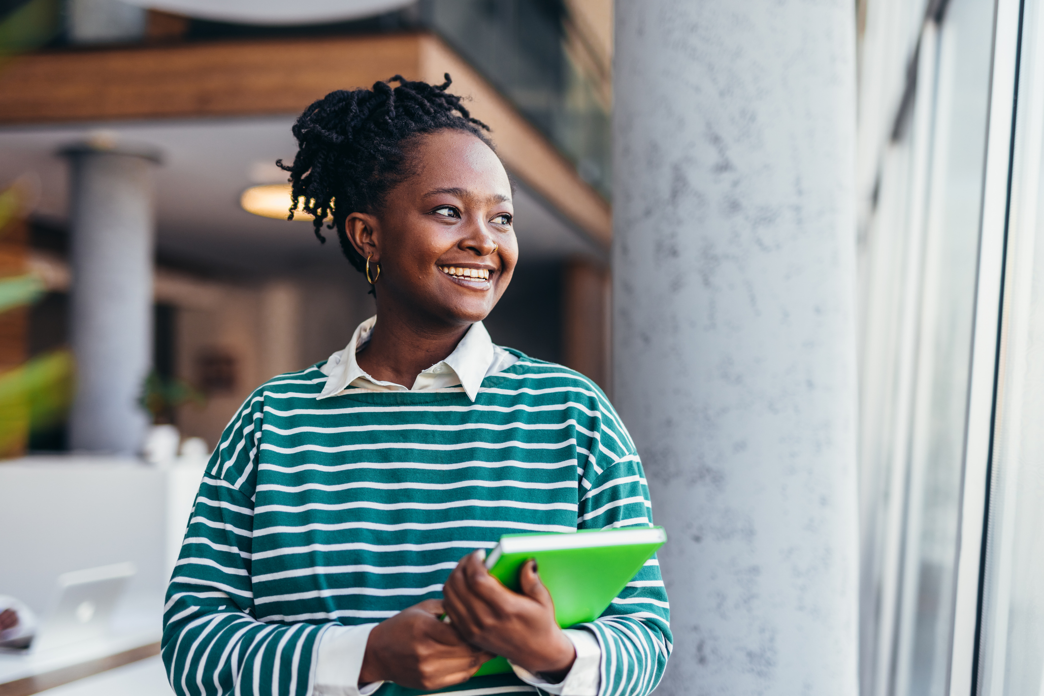 Young black female student smiling and holding a book in university hall
