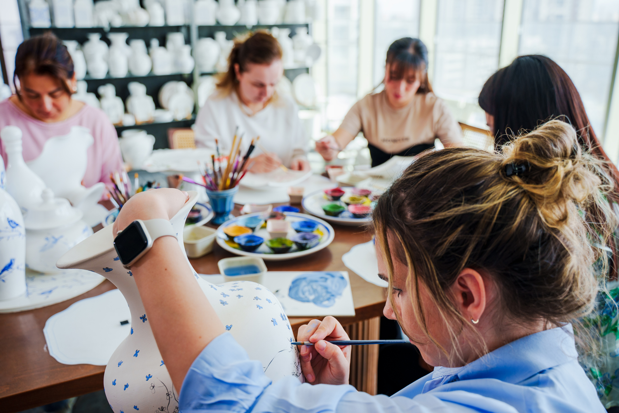 A group of people of different races and ages take part in a tile painting therapy class