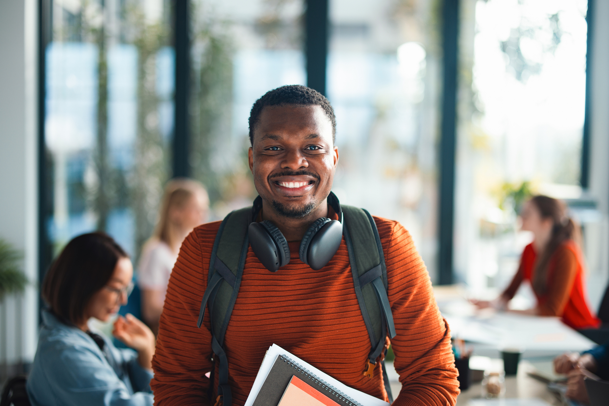 Smiling Student With Backpack and Headphones Holding Notebooks in University Library Study Group