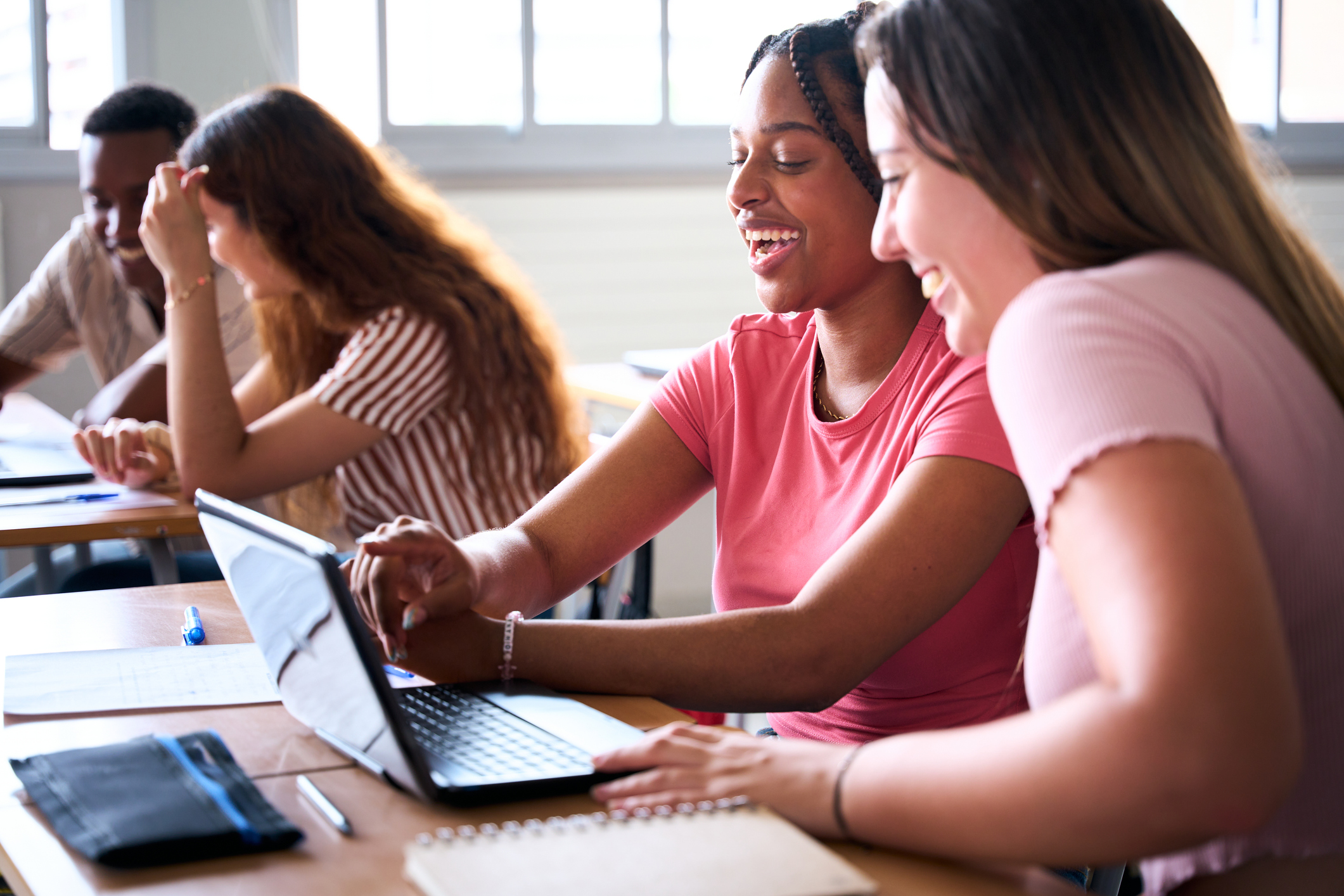 Cheerful female students sharing laptop in university
