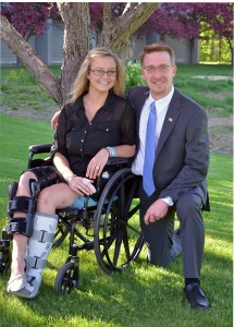 Alexis Maillet sitting in her wheelchair and Christopher Brown kneeling beside her under a tree