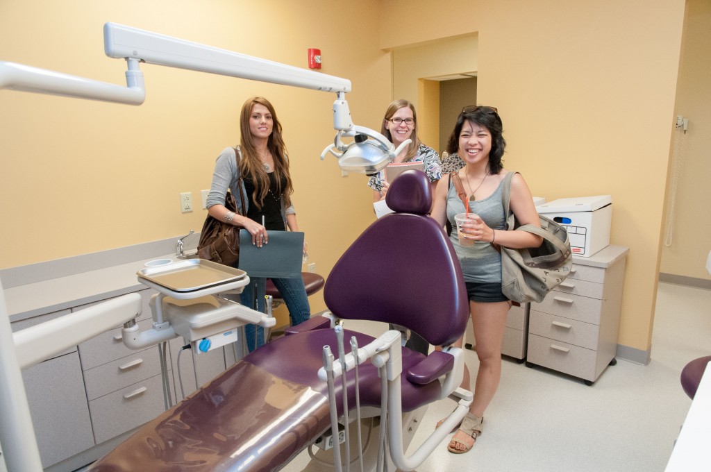 Three dental students touring the new Dental Labs [a dentist's chair in the foreground]