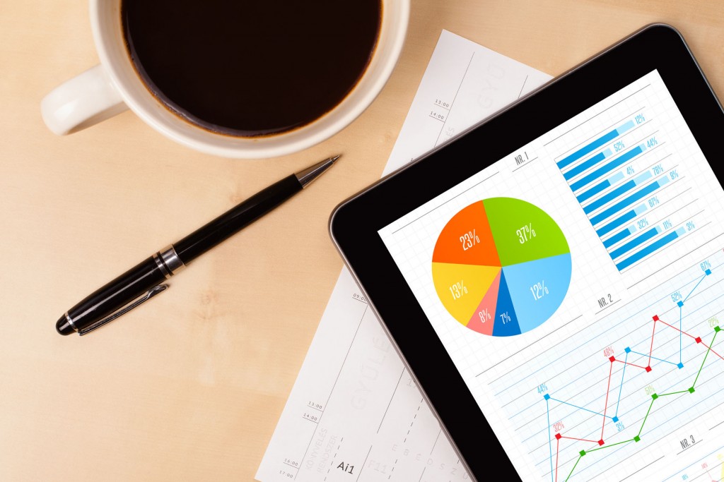 Business items on a desk [coffee, pen, report, ipad with charts on the screen]