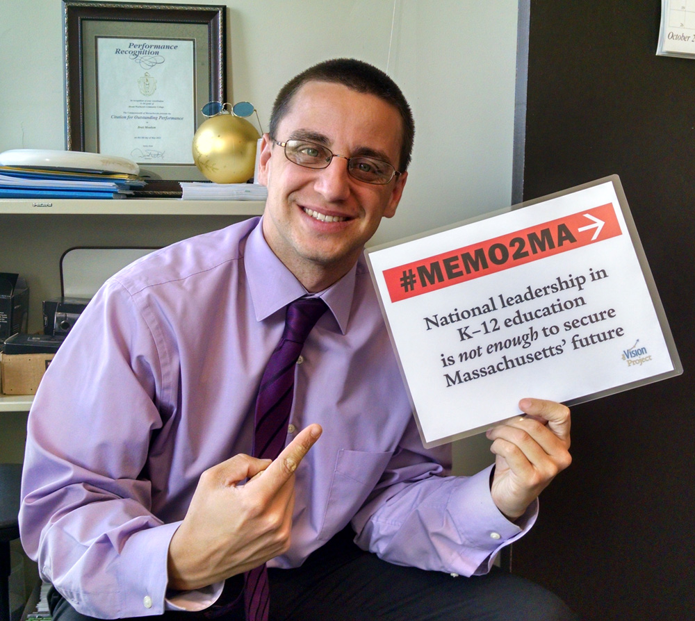 Professor Shawn Case holding a sign that says "#MEMO2MA National Leadership in K-12 education is not enough to secure Massachusetts' future"