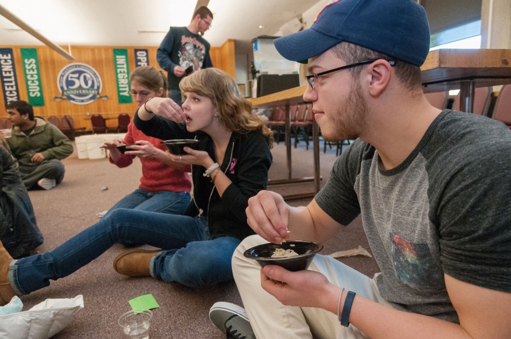 Group of students eating rice out of bowls with their hands