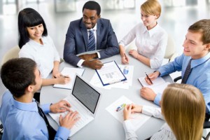 Stock photo of a diverse business group sitting around a table with reports and a laptop on it