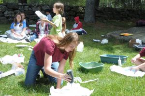 Jess Higbee working on an art project in the grass with kids in the background