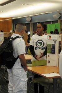 Two students talking together in front of a club presentation board